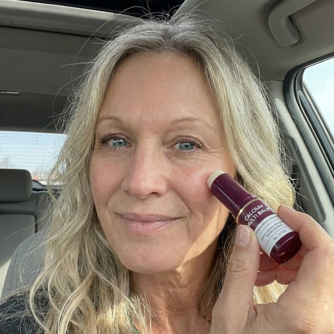 Person in car applying beauty balm to cheek.